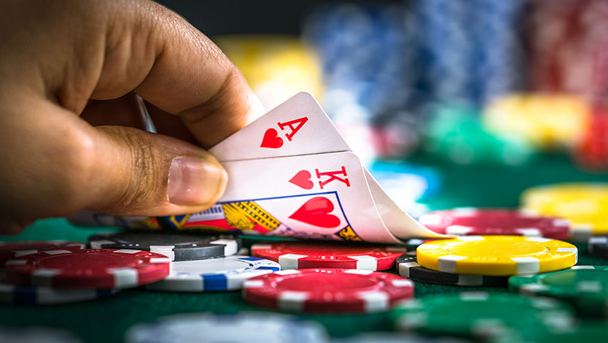 Hand tipping up Ace and King of Hearts with poker chips underneath