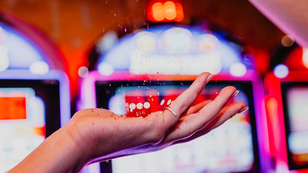 Hand Holding Dice With Slot Machines In The Background